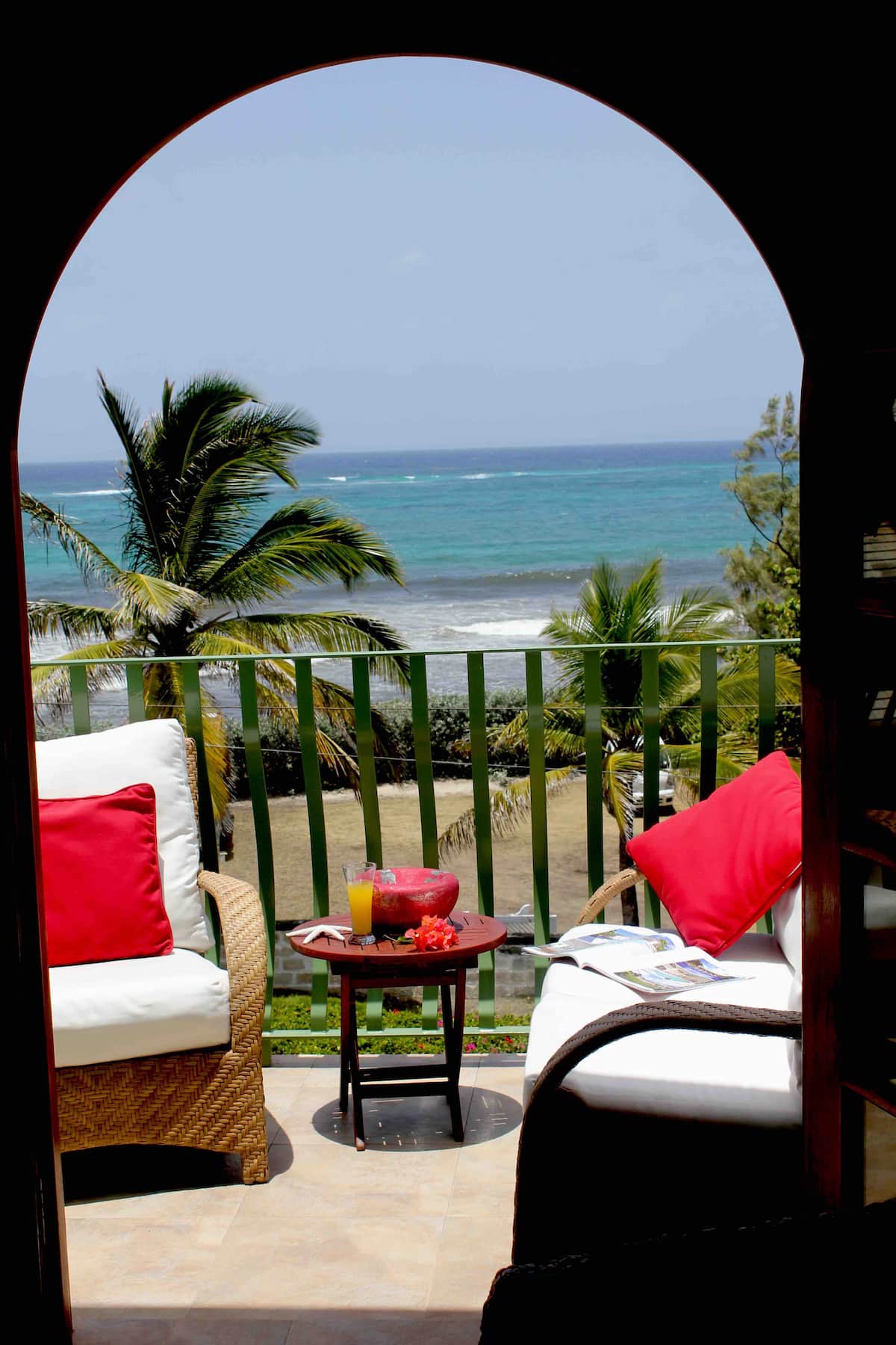 Two balcony chairs beneath an arch overlooking palms and ocean at Sea Mist